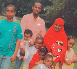 Mohamed, his wife Safia, and their six children stand smiling in a park.