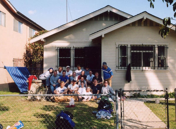 2002 - A group of AmeriCorps members sitting outside of a finished house in the front yard, behind a chain-link fence.