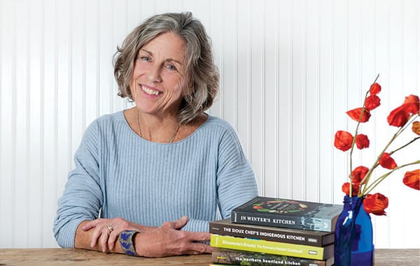 Chef Beth Dooley next to a stack of her books and some red flowers.