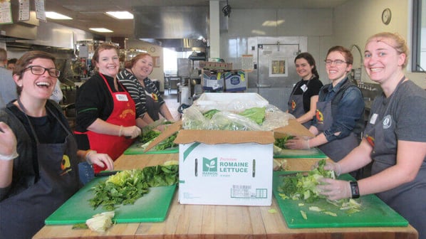 Volunteers chopping lettuce at a long table.