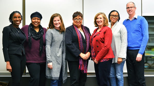 The CDFI Advisory Council, seven members, standing angled toward each other in a hallway, smiling.