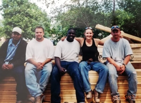 Heather and four men from Sentencing to Service sitting on a pile of wooden beams outside.