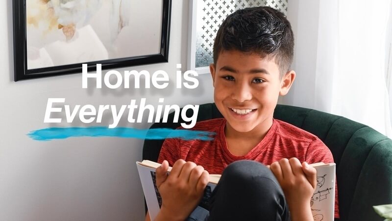 A young boy reading a book in a chair in his Habitat home, with the text "Home is Everything" in white.