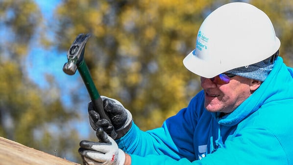 Chris Coleman in a blue Habitat sweatshirt and hard hat, hammering a roof outside.