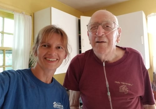 Lynda and Ken smiling and standing in Ken's kitchen. Lynda's wearing a blue TC Habitat shirt and Ken is wearing a red Holy Hammers shirt.