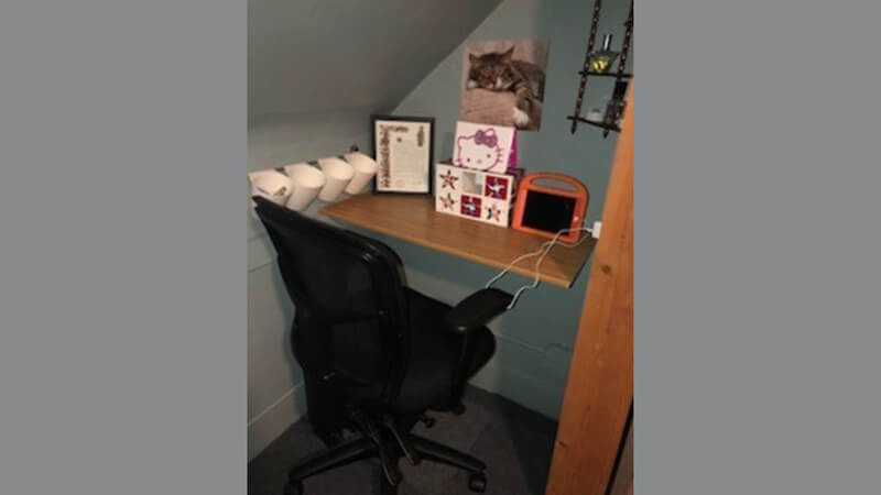 Laurie's desk with a rolling desk chair, a photo of a cat, Sanrio artwork, various other art, a touchscreen pad, and organizer cups.