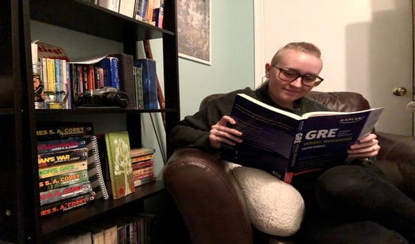 Mikayla sitting in a leather chair by a bookshelf, reading a GRE study guide.