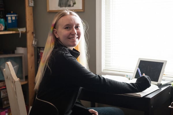 Mikayla studying in her room in front of a book and tablet computer.