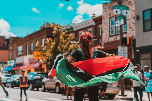 A woman wears the pan-Afridan flag as a shawl in the street during a Juneteenth celebration.