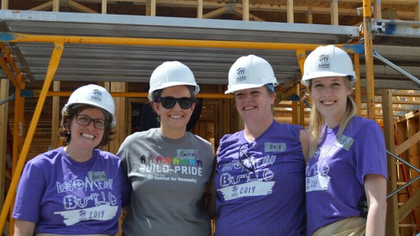 Four volunteers wearing Women Build and Build Pride shirts in front of an in-progress house.