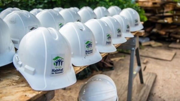 Three rows of white Twin Cities Habitat hard hats on a workbench.