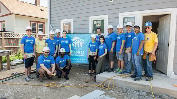 A group of General Mills volunteers outside of an in-progress house, with a Twin Cities Habitat sign behind them.