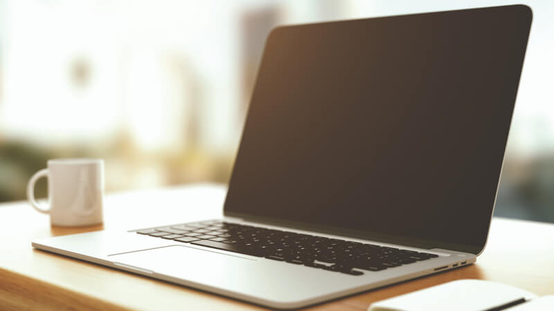 A laptop with a coffee mug on a desk.