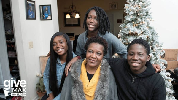 Melo and her three children in front a Christmas tree in their living room, smiling.