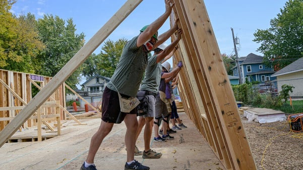 Five volunteers working together to push a wall up into place on as they frame a house.