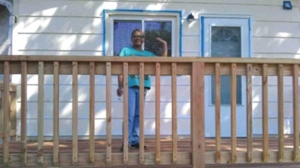Nevonne, in a green t-shirt and blue jeans, smiling and waving on her new deck.