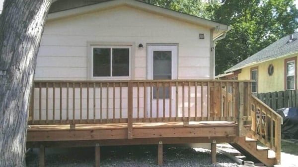 The back of Nevonne's house, with one window, and the back door leading out onto the newly finished deck and stairs leading down to the ground.