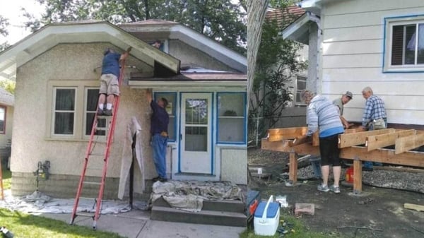 Two images. The first - Two volunteers working on the underside of the roof at the front of the house. The door and windows have blue tape on them, there are drop cloths on the ground, and one of the volunteers is standing on an orange ladder. The second - Three volunteers work on the base of the deck in the back yard, with a cooler in the foreground and tape around the windows.