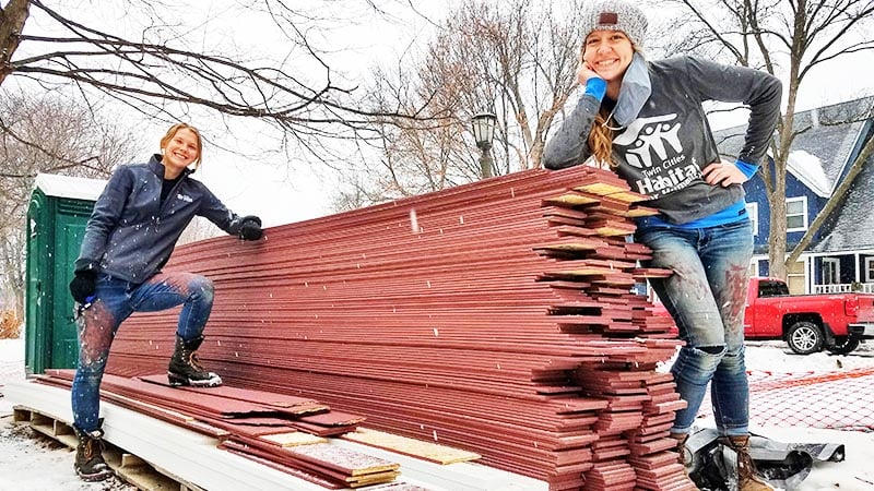 Two members of the homebuilding team posing with a pile of lumber.