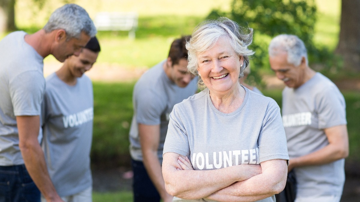 small group of happy retirees volunteering outside wearing grey volunteer shirts.