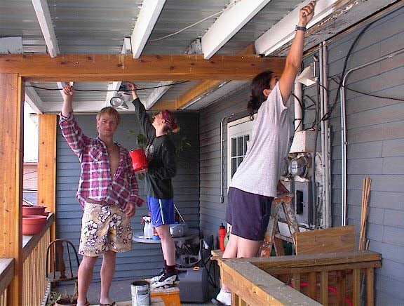 Three AmeriCorps members painting the porch of the Fourplex.