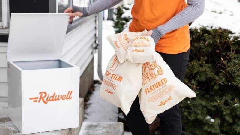 A person with an orange shirt putting bags into a white box that says
