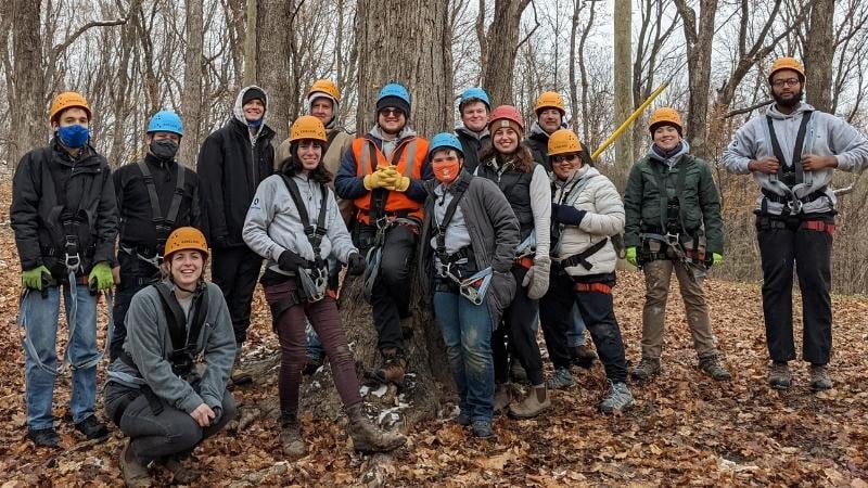Group of AmeriCorps members in the woods in fall, wearing harnesses for a ropes course