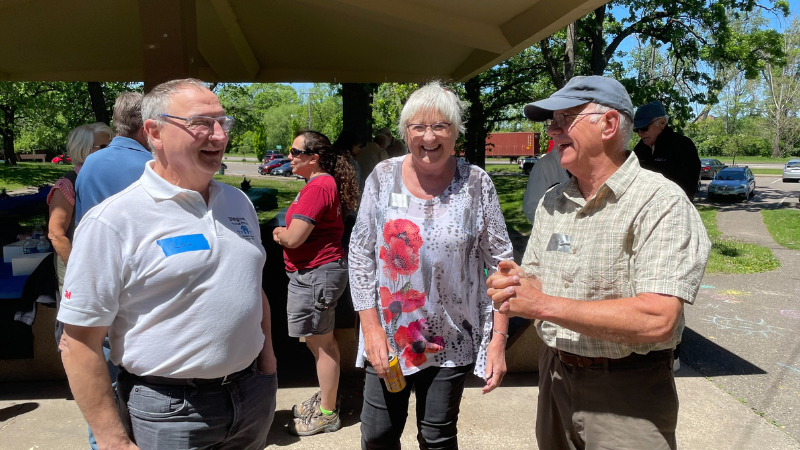 Three Volunteer Emeritus laughing under a picnic shelter in the sun.