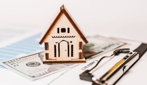 wooden house on clipboard next to pen and money