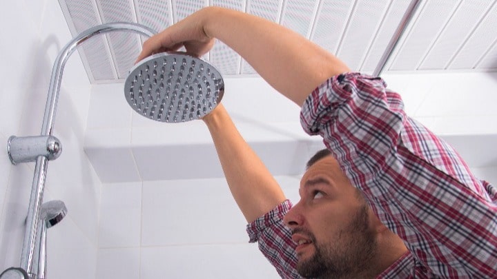 A bearded person replacing a shower head.