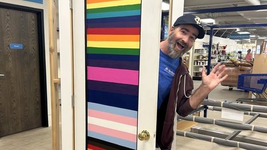 ReStore Assistant Manager Robert with his door painted with a variety of Pride Month flags.