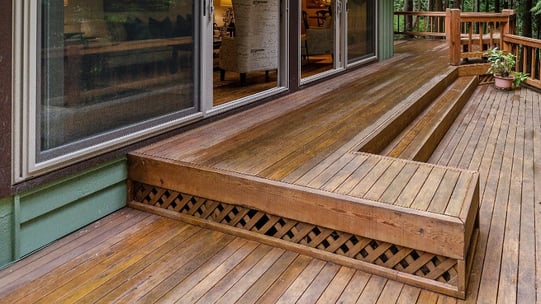 A newly-stained deck outside of a green house.
