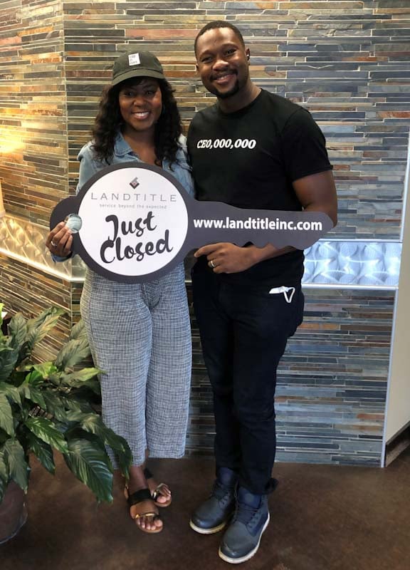 Monisha and her husband at her home closing, smiling and holding her house keys and an oversized cardboard cutout of a key.
