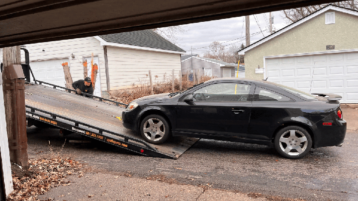 A black Chevy Cobalt is loaded onto a tow truck