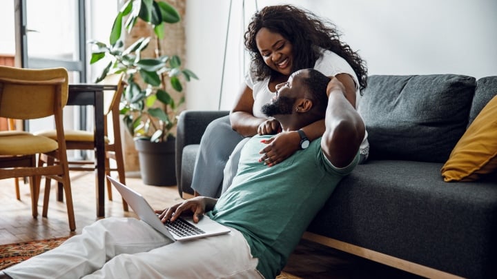 Homeowner couple smiling at each other on a couch.