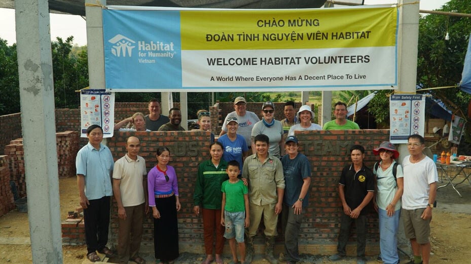 A group of people stand in front of a Habitat for Humanity Vietnam sign