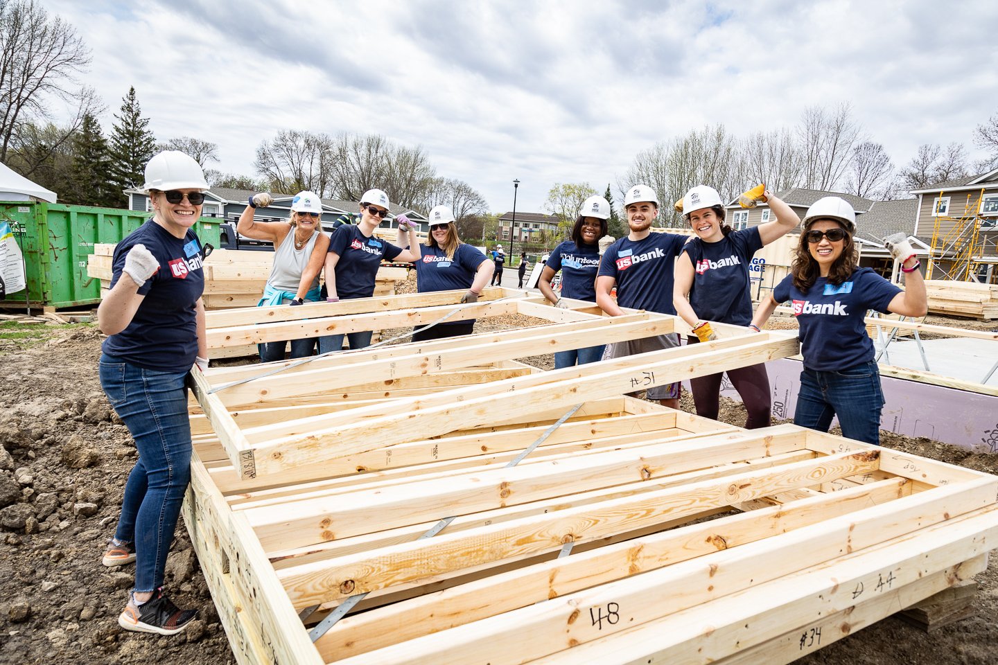 US Bank employees lifting a wall frame while smiling and flexing their arms.