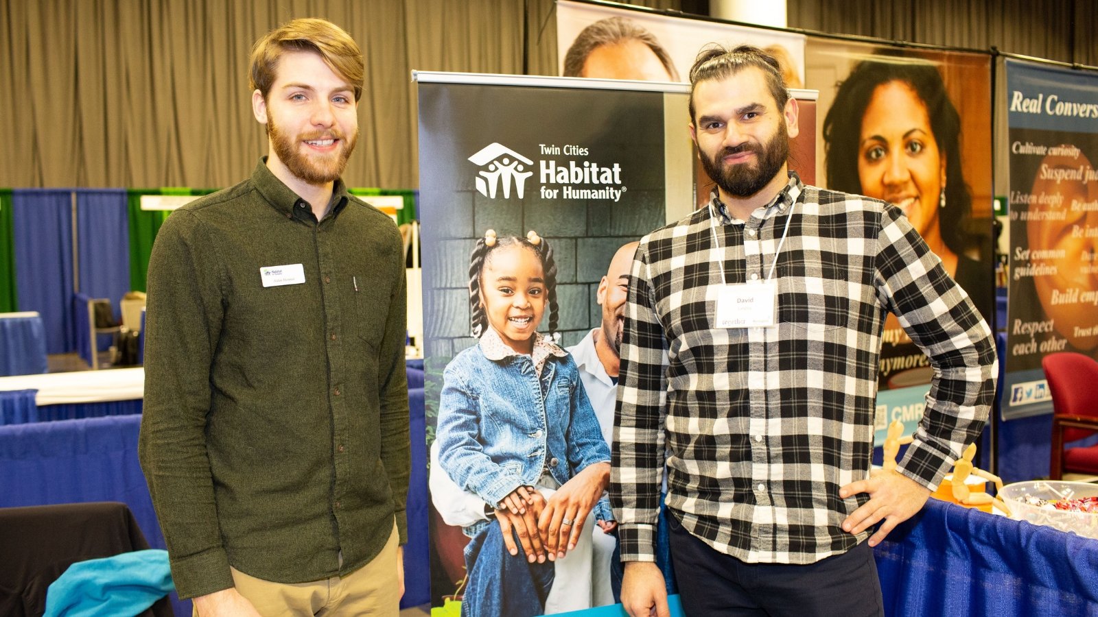 Two AmeriCorps Members at an event standing in front of a Habitat banner