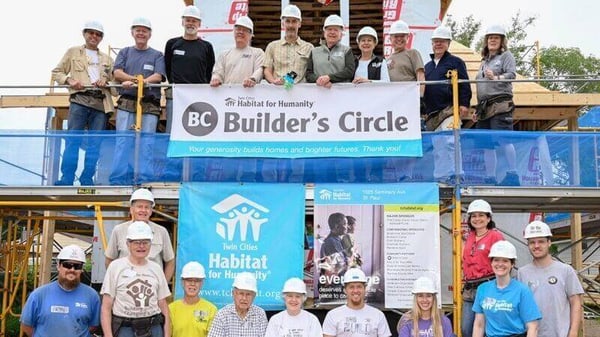 A group from the Builder's Circle Build standing around the Builder's Circle and TC Habitat signs.