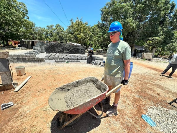 Chris Coleman carrying a wheelbarrow of concrete.