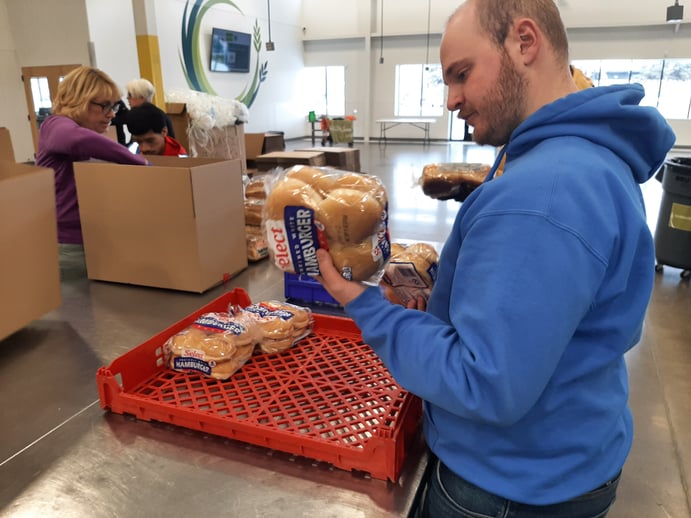 An AmeriCorps Member inspecting a package of hamburger buns to ensure that they are safe to go out Second Hand Harvest's affiliates. 
