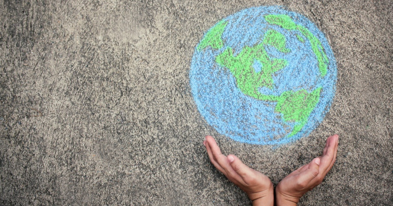 Two hands cupping a chalk drawing of the planet earth on a sidewalk.