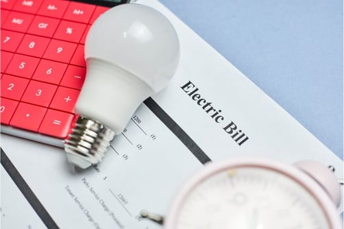 An electric bill, calculator, and light bulb grouped on a table.