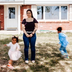 Linda standing in front of her house while her kids run around her.