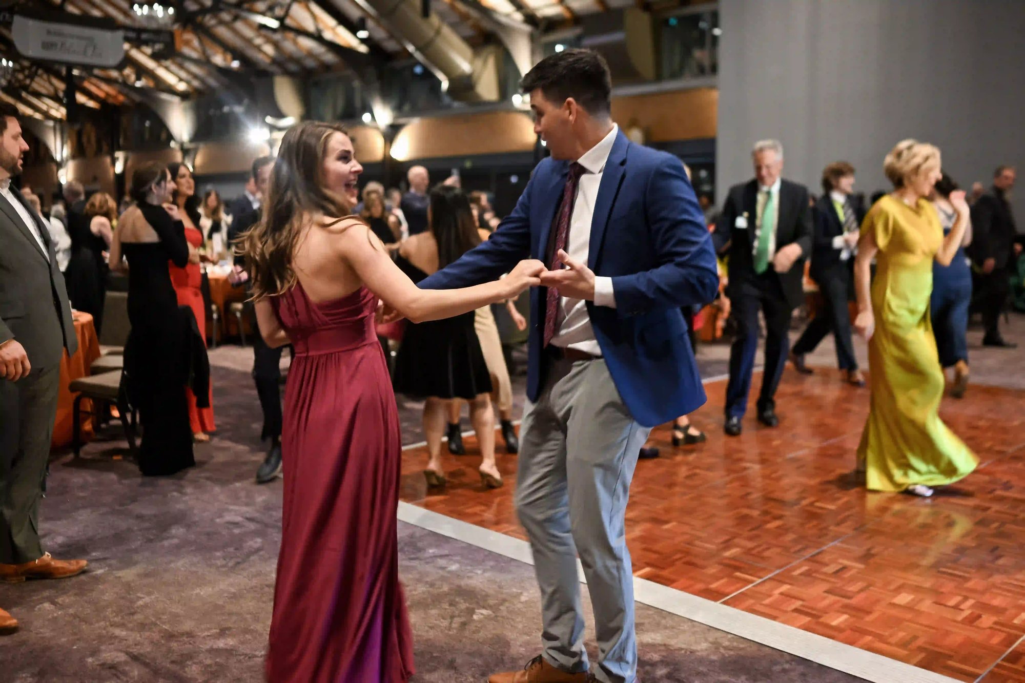 A couple in a red gown and gray and blue suit dancing and laughing.