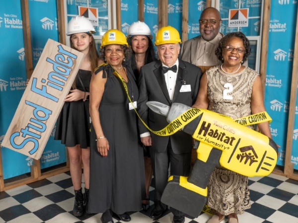 Group of gala attendees smiling at the photo booth and holding large photo props, such as a large yellow drill.