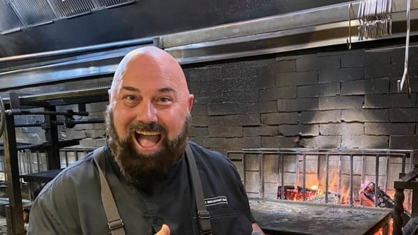 Chef Brian Ingram smiling in front of a fire pit.