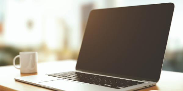 A silver laptop and white coffee mug sitting on a desk.