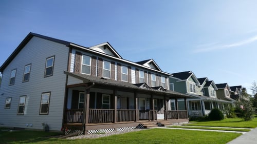 A two-story Habitat duplex with white siding and brown trim, next to several other houses.