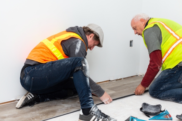 Two volunteers laying flooring planks.